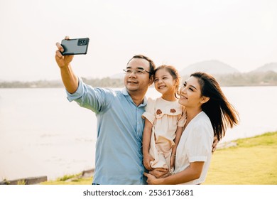 Asian family taking selfie picture with smartphone outdoor nature park, Happy smile father mother and child daughter taking photo with mobile phone together, Tourist lifestyle people leisure activity - Powered by Shutterstock