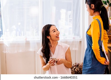 Asian Family Of Teen Daughter Giving Paper Postcard As Gift To Mature Mother At Home On Daytime. Female Teenager Surprises Mature Woman