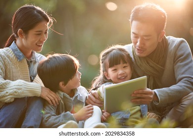 Asian Family With Two Children Relaxing Outdoors In City Park