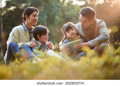 Asian Family With Two Children Relaxing Outdoors In City Park