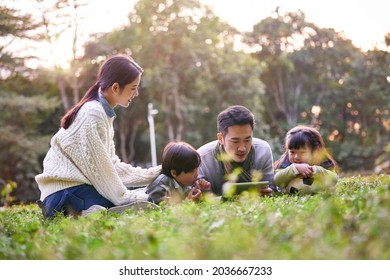 Asian Family With Two Children Relaxing Outdoors In City Park