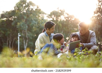 asian family with two children relaxing outdoors in city park - Powered by Shutterstock