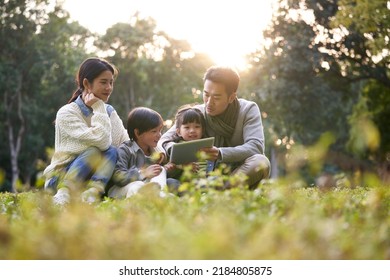 Asian Family With Two Children Relaxing Outdoors In City Park