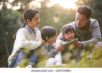 Asian Family With Two Children Relaxing Outdoors In City Park