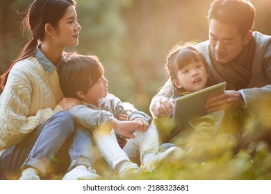 Asian Family With Two Children Relaxing Outdoors In City Park