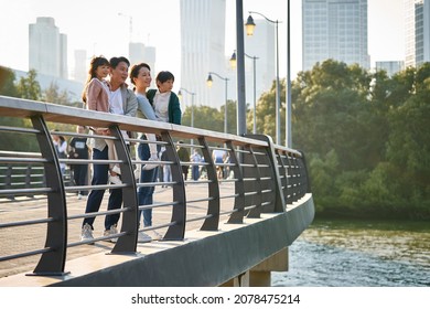asian family with two children standing on pedestrian bridge looking at view in city park