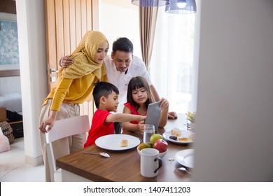 Asian Family Using Tablet Pc At Home During Breakfast In The Morning