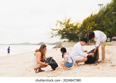 Asian Family Volunteers And Children Collecting Garbage On The Beach. Group Of Environmental Help To Keep Nature Clean Up And Pick Up Garbage. Concept Of Conservation And Pollution Problems.