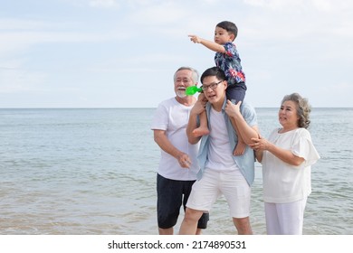 Asian Family Walking On The Beach Together. Son Sitting On Father's Shoulder With Support From Grandmother And Grandfather. Travel Vacation On Summer