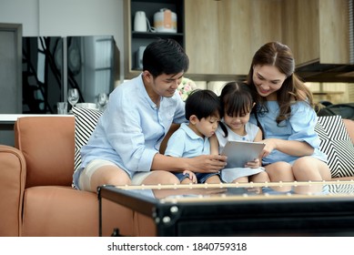 Asian family young parents sit on couch with daughter and son have fun using tablets together to watch funny videos in living room at home. Activities together and relationships in family concept. - Powered by Shutterstock