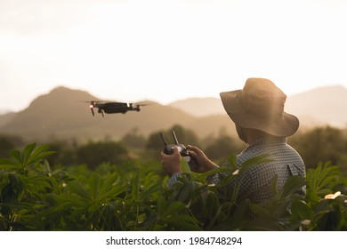 Asian Farmer Using Drone Flying Navigating Above Farmland. A Young Farmer Controls A Drone In A Large Scale Survey Of Agricultural Plots For Modern Farming And Farming.