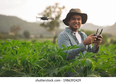 Asian Farmer Using Drone Flying Navigating Above Farmland. A Young Farmer Controls A Drone In A Large Scale Survey Of Agricultural Plots For Modern Farming And Farming.