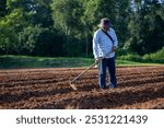 Asian farmer is using hoe to plough tilled soil ready for planting in the countryside during summer for potato plantation and agriculture concept