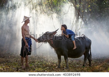 Asian farmer watching his daughter ride on a buffalo.