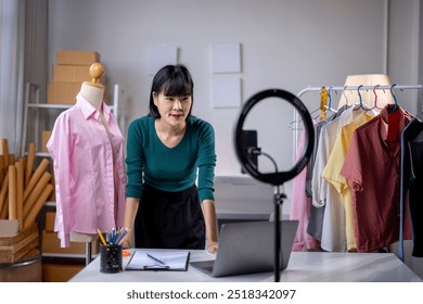 Asian fashion designer presenting new clothes collection using smartphone streaming online from home office - Powered by Shutterstock