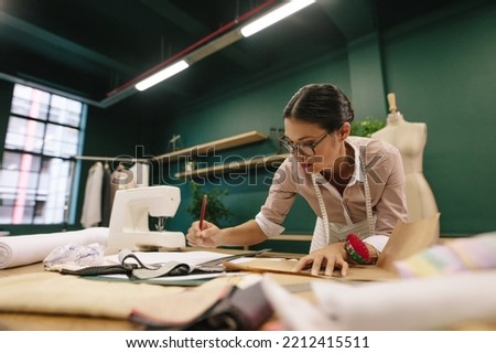Asian fashion woman designer drawing design sketch. Female designer working in her fashion studio.