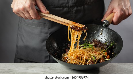 Asian Fast Food Rice Clear Noodles Cooking With Fried Meat And Spicy Vegetables By Cook Chef Hands In Wok Pan. Close Up Food Recipe Concept.