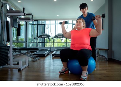 Asian Fat Girl Work Out And Weight Lifting On A Rubber Ball With Her Trainer, This Image Can Use For Fat, Diet, Fitness And Exercise Concept