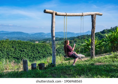 Asian fat guy sitting on wooden swing with Beautiful landscape view on Phu Lamduan at loei thailand.Phu Lamduan is a new tourist attraction and viewpoint of mekong river between thailand and loas. - Shutterstock ID 1906968565