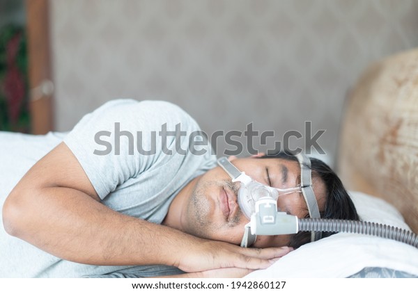 Asian fat man wearing Cpap mask sleeping in bed, snoring\
man.Obstructive sleep apnea therapy. Cpap therapy, medical health,\
Sleep test, Good sleep, Machine, Patient, Sleep Disordered\
Breathing.Sdb 
