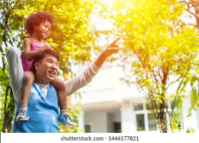 Asian Father And Adopted Child Or Daughter  On Nature On Sunset, Diversity Family Or Mixed Race Parents Carrying Kid On Shoulders As They Walk In Park. Concept Of Happy Family Spending Good Time