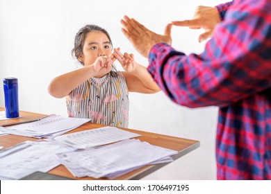 Asian father is communicating with a deaf daughter, paying attention to the child who is sitting on a chair in the living room.She is doing homework Hearing loss, deaf, disabled, sign language concept - Powered by Shutterstock