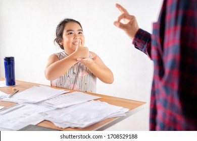 Asian father is communicating with a deaf daughter, paying attention to the child who is sitting on a chair in the living room.She is doing homework Hearing loss, deaf, disabled, sign language concept - Powered by Shutterstock