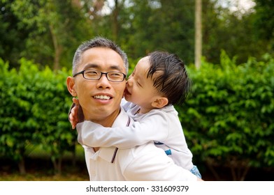 Asian Father Giving Piggyback Ride To His Son In The Evening Sunshine