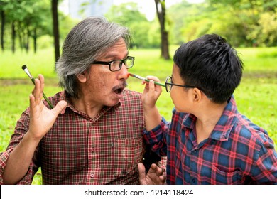 Asian Father Or Grand Father Playing Paint Face Together With Son Or Grand Son In The Park