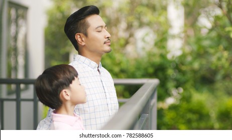 Asian Father And His Son Standing On Balcony Enjoying Fresh Nature