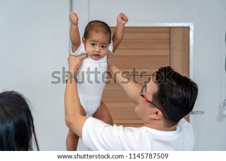 Asian father holding the boy baby Raising hands and mother hand in the house, Family Lifestyle Concept