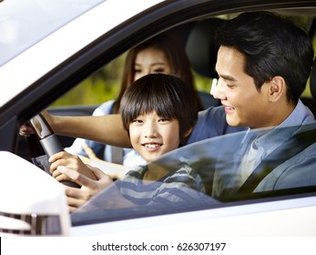 Asian Father Letting His Son Hold The Steering Wheel Of His Car.