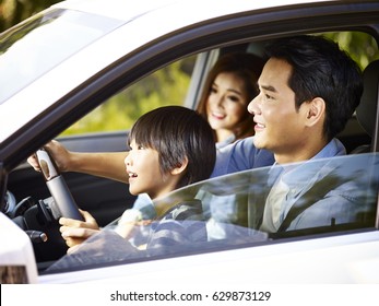 Asian Father Letting His Son Hold The Steering Wheel Of His Car.