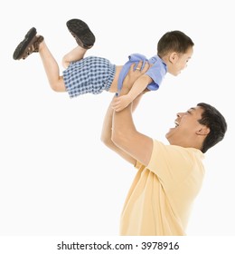 Asian father lifting son up into air in front of white background.
