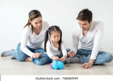 Asian Father Mother And Daughter, Parents Are Teaching Children To Save Money. Family Saving Money Putting Coins Into Pig Bank