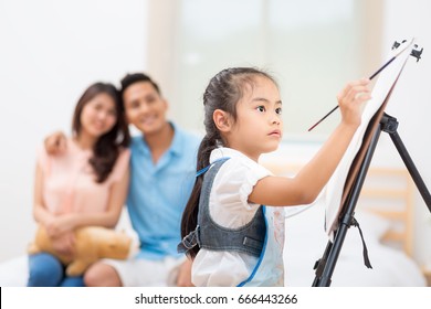 Asian Father And Mother Looking Daughter Child Painting With Watercolor On The Easel At Home.Kids And Happy People Concept,Family Concept.