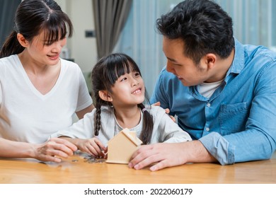 Asian Father And Mother Teach Young Daughter To Save Money For Future. Happy Little Girl Enjoy Put Coins In Piggy Bank With Parents And Learn To Manage Financial Plan. Loving Family Couple Concept.