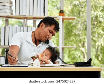 Asian father multitasks by feeding his baby while working on documents and talking on phone in home office - Powered by Shutterstock