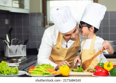 Asian Father With Son In Chef Hat Apron Helping  Prepare Cooking Fresh Salad Food In Kitchen At Home.Cute Little Boy With Handsome Dad Cooking Together.Family Healthy Lifestyle Concept