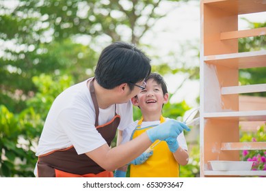 Asian Father And Son Painting Wooden Shelf Together