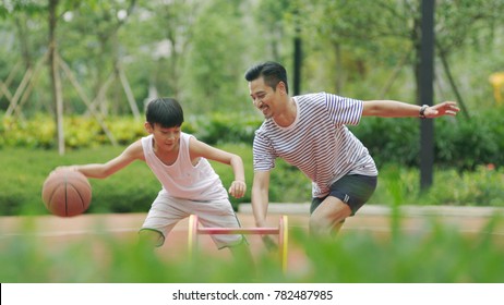 Asian Father & Son Playing Basketball In Garden In Morning