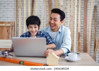 Asian father and son using laptop computer together in carpentry workshop. Concept family doing hobby at home.