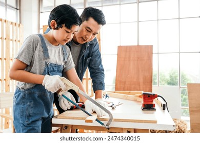 Asian father and son work as a woodworker or carpenter, Father teaches his son to saw a wooden plank with hack saw carefully together with teamwork. Craftsman carpentry working at home workshop studio - Powered by Shutterstock