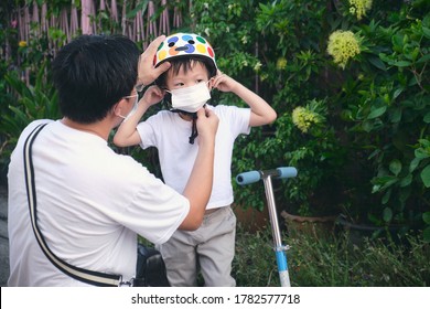 Asian Father Spending Time With Little Son Riding Scooter In City, Parent Putting Mask On His Toddler Boy Child During Covid-19 Outbreak, New Normal Lifestyle Concept, Selective Focus