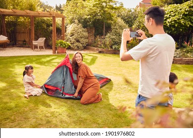 Asian Father Taking Photo On Mobile Phone As  Put Up Tent Family In Garden At Home