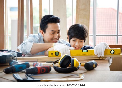 Asian Father Teach Son Using Level Tool For Measure Surface Of Timber In Carpentry Workshop. Concept Family Doing Hobby Together At Home.