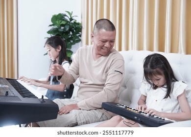 Asian father teaches two daughters to play the electric tone together, both of them practice playing music and singing, sitting on the sofa in the living room and having a good relationship in the hou - Powered by Shutterstock