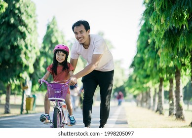 Asian Father Teaching Daughter To Ride Bike In The Park