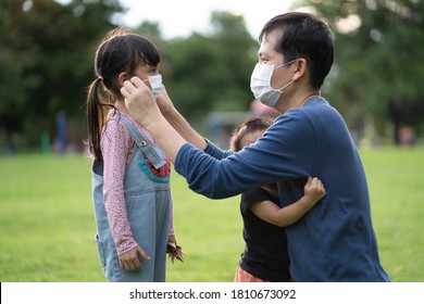 Asian Father Is Wearing The Face Mask For Little Daughter While The Are Enjoying For Outdoor Activity, Concept Of Social Distancing And Using Of Ppe In The Public Place In The Covid19 Virus Outbreak.