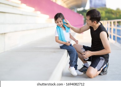 Asian Father Is Wiping Sweat For The Little Daughter And They Talking And Smile Together While Resting For Jogging Time, Concept Of Parent Care And Support For Kid Outdoor Activity On Family Lifestyle